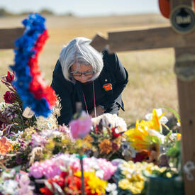 La gouverneure générale Mary Simon dépose quelque chose sur un monticule de fleurs. Il y a une croix floue au premier plan.