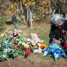 La gouverneure générale Mary Simon est agenouillée auprès d’une tombe couverte de fleurs.