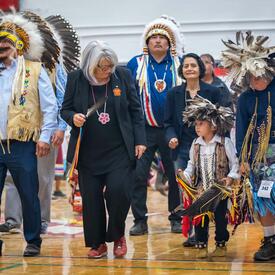 La gouverneure générale est debout dans le gymnase. Elle tient une plume et regarde un jeune enfant à sa gauche.