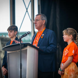 Le lieutenant-gouverneur de la Saskatchewan, Russ Mirasty, est sur scène avec des étudiants de chaque côté de lui.