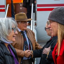La gouverneure générale parle à l'ambassadrice canadienne en Islande, Jeannette Menzies. M. Fraser et trois autres personnes se tiennent derrière eux sur le tarmac. Le côté d'un avion est visible derrière eux.