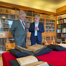 M. Fraser se tient à côté de M. Gudvardur Mar Gunnlaugsson. Ils parlent. Un grand manuscrit aux pages patinées est ouvert devant eux.