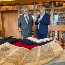 M. Fraser se tient à côté de M. Gudvardur Mar Gunnlaugsson. Ils parlent. Un grand manuscrit aux pages patinées est ouvert devant eux.