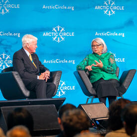 La gouverneure générale parle à M. Ólafur Ragnar Grímsson. Ils sont assis l'un à côté de l'autre dans des fauteuils noirs.