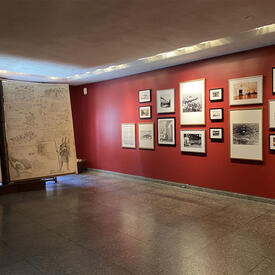 There is a large 2-piece display of sketches and text on the left. A red wall featuring a mix of 17 photographs, sketches and paintings is on the right.