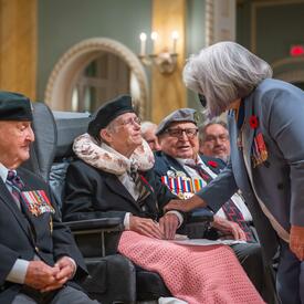The Governor General speaks with an individual who is seated in a wheelchair. There is a group of people seated around them.