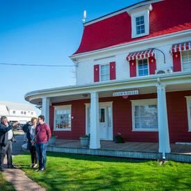 La gouverneure générale se tient à l'extérieur avec un petit groupe de personnes. Il y a un bâtiment rouge et blanc derrière eux.