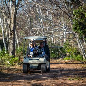 La gouverneure générale est conduite à travers les bois dans une voiturette de golf.