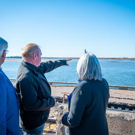 La gouverneure générale parle à quelqu'un en regardant l'eau. Un homme montre quelque chose du doigt.