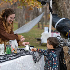 A child is looking at a Halloween decorating table. A member of the Rideau Hall staff is holding a small jar.