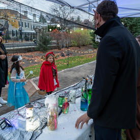 Young kids dressed up for Halloween are looking at a table with Halloween displays. 