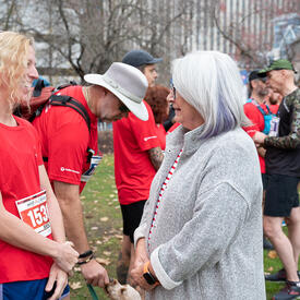 Governor General Mary Simon is speaking with a participant of the Army Run. They are standing outside and there are many other participants around them. 