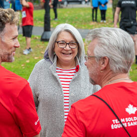 Governor General Mary Simon is speaking with two participants of the Army Run. She is smiling. The photo is taken from behind the two participants.
