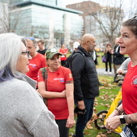 La gouverneure générale Mary Simon parle avec une participante à la Course de l'Armée. Elles sont debout à l'extérieur et il y a beaucoup d'autres participants autour d'eux. 