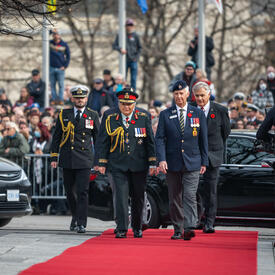 La gouverneure générale marche sur un tapis rouge en direction du Monument commémoratif de guerre du Canada. Elle porte l'uniforme de l'armée canadienne.