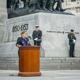 Un padre militaire s'exprime sur un pupitre devant le Monument commémoratif de guerre du Canada.