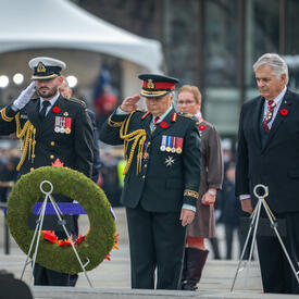 Governor General Mary Simon is saluting after placing a wreath on a stand at the National War Memorial in Ottawa. Several people are standing behind her.