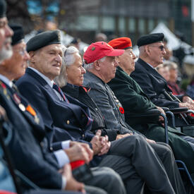 Des gens assis en rangs dehors. Beaucoup d'entre eux portent des uniformes militaires.