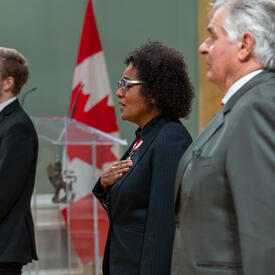  The Right Honourable Michaëlle Jean is holding her hand to her heart while singing the National Anthem.
