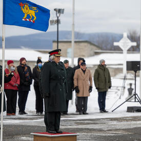 The Governor General is standing outside on a small podium. The Governor General flag hangs on a flag pole to her right.
