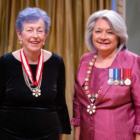 La gouverneure générale Simon se tient à côté d’une femme qui porte une médaille autour du cou.