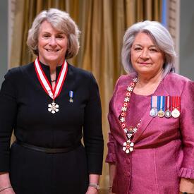 Governor General Simon is standing next to a woman who has a medal hanging around her neck.