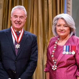 Governor General Simon is standing next to a man who has a medal hanging around his neck.