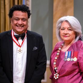 La gouverneure générale Simon se tient à côté d’un homme qui porte une médaille autour du cou.