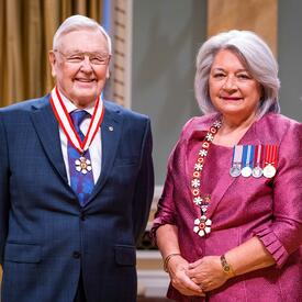 La gouverneure générale Simon se tient à côté d’un homme qui porte une médaille autour du cou.