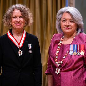 Governor General Simon is standing next to a woman who has a medal hanging around her neck.