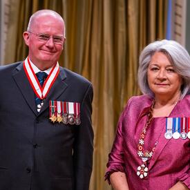 La gouverneure générale Simon se tient à côté d’un homme qui porte une médaille autour du cou.