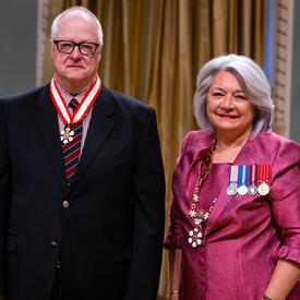 La gouverneure générale Simon se tient à côté d’un homme qui porte une médaille autour du cou.
