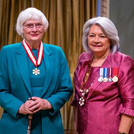 La gouverneure générale Simon se tient à côté d’une femme qui porte une médaille autour du cou.