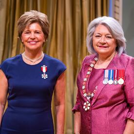 La gouverneure générale Simon se tient à côté d’une femme qui porte une médaille épinglée à sa robe bleue..