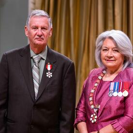 Governor General Simon is standing next to a man who has a medal pinned to his black blazer.