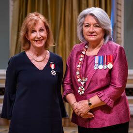 Governor General Simon is standing next to a woman who has a medal pinned to her blue dress.