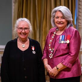 La gouverneure générale Simon se tient à côté d’une femme qui porte une médaille épinglée à son habit noir.