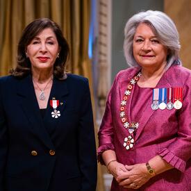 La gouverneure générale Simon se tient à côté d’une femme qui porte une médaille épinglée à son blazer bleu.