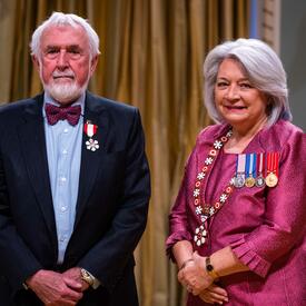 La gouverneure générale Simon se tient à côté d’un homme qui porte une médaille épinglée à son blazer bleu.