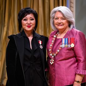 La gouverneure générale Simon se tient à côté d’une femme qui porte une médaille épinglée à son manteau noir.