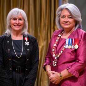 La gouverneure générale Simon se tient à côté d’une femme qui porte une médaille épinglée à son blazer noir.