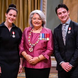 Governor General Simon is standing between a man and a woman who have medals pinned to their shirt and blazer..