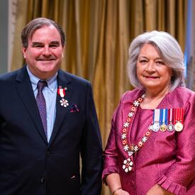 La gouverneure générale Simon se tient à côté d’un homme qui porte une médaille épinglée à son blazer bleu.