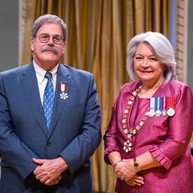 La gouverneure générale Simon se tient à côté d’un homme qui porte une médaille épinglée à son blazer bleu.