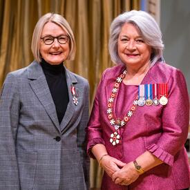 Governor General Simon is standing next to a woman who has a medal pinned to her grey blazer.