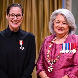 La gouverneure générale Simon se tient à côté d’une femme qui porte une médaille épinglée à sa chemise noire.