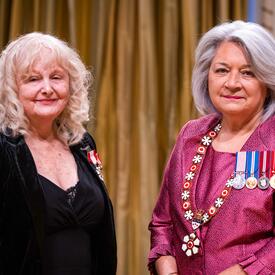 Governor General Simon is standing next to a woman who has a medal pinned to her black blazer.