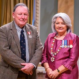 La gouverneure générale Simon se tient à côté d’un homme qui porte une médaille épinglée à son blazer brun pâle.