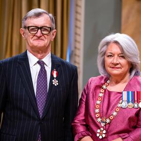 La gouverneure générale Simon se tient à côté d’un homme qui porte une médaille épinglée à son blazer noir.
