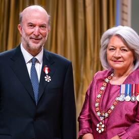 La gouverneure générale Simon se tient à côté d’un homme qui porte une médaille épinglée à son blazer bleu.